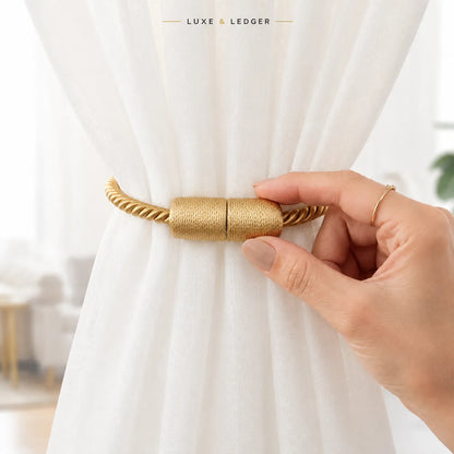 A close-up of a hand holding a gold rope-style curtain tieback against a white sheer curtain, with the brand name 'LUXE & LEDGER' at the top.