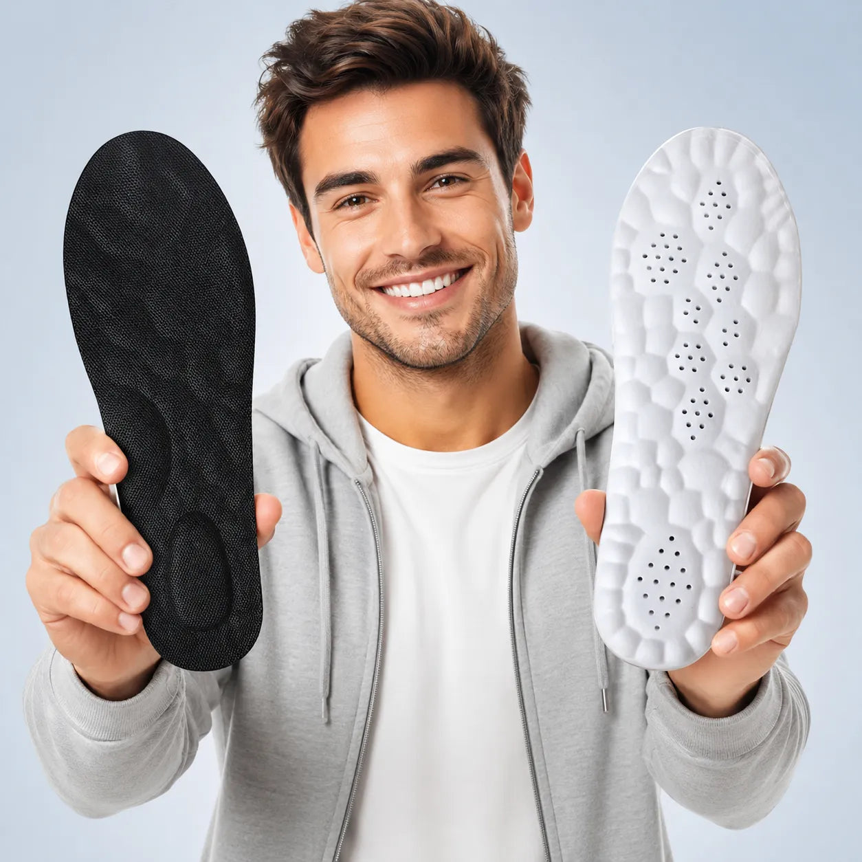 Man holding black and white shoe insoles against a light gray background