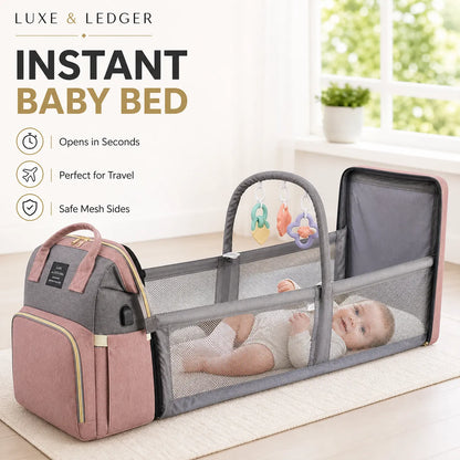 Portable baby bed with pink and gray design, featuring a baby inside, on a light wooden floor.