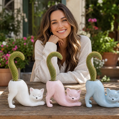 Woman sitting behind three cat-shaped planters with cacti on a wooden table.