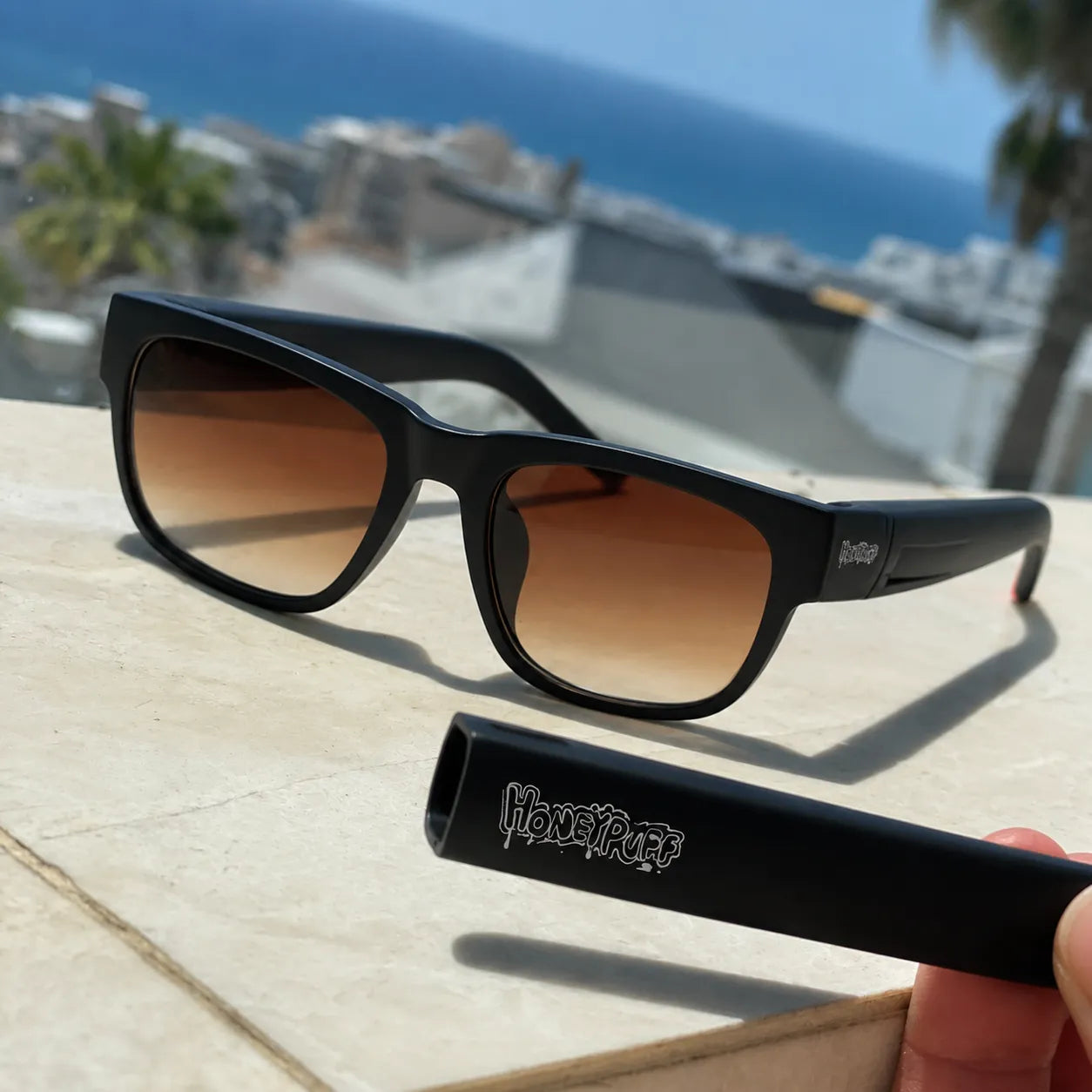 Black sunglasses with gradient lenses on a wooden surface, with 'Honey Pure' branding.