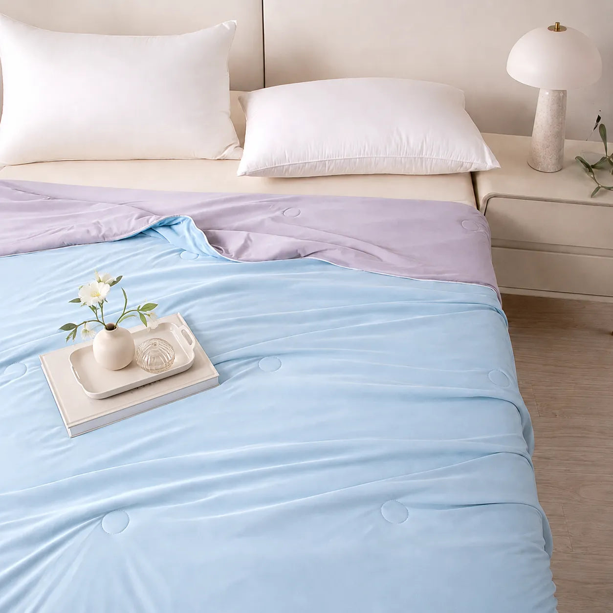 Bed with light blue and purple bedding, white pillows, and a small table with decor items.