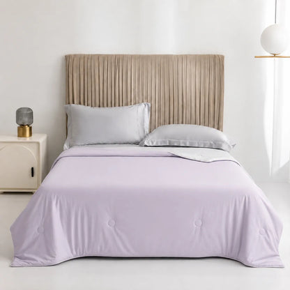 Bed with lavender comforter and pillows in a bedroom setting