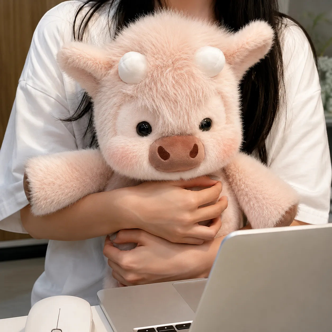 Person holding a pink plush pig toy in front of a laptop.