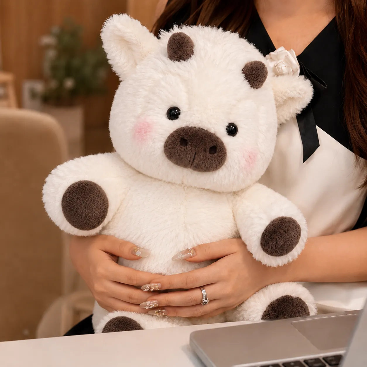 Person holding a white teddy bear with brown paws and ears in an indoor setting.