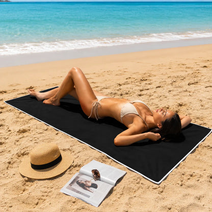 Woman lying on a black beach mat with a hat and magazine at the beach.