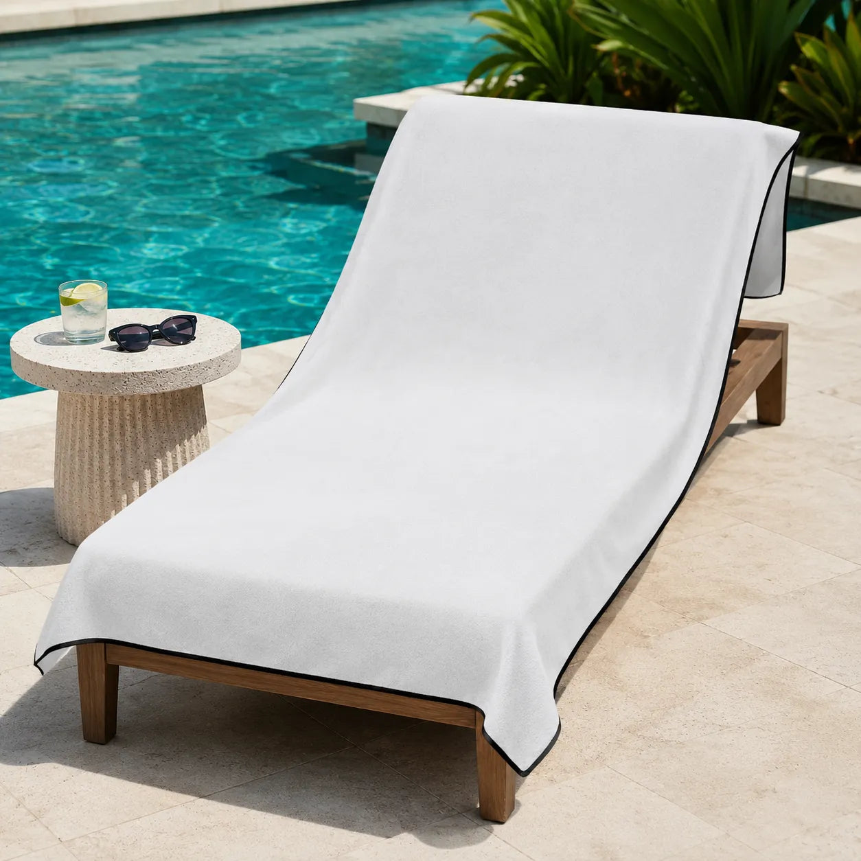 White towel draped over a lounge chair by a poolside with sunglasses and a drink.