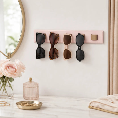 Pink sunglasses holder with four pairs of sunglasses on a white wall, next to a mirror and decorative items.