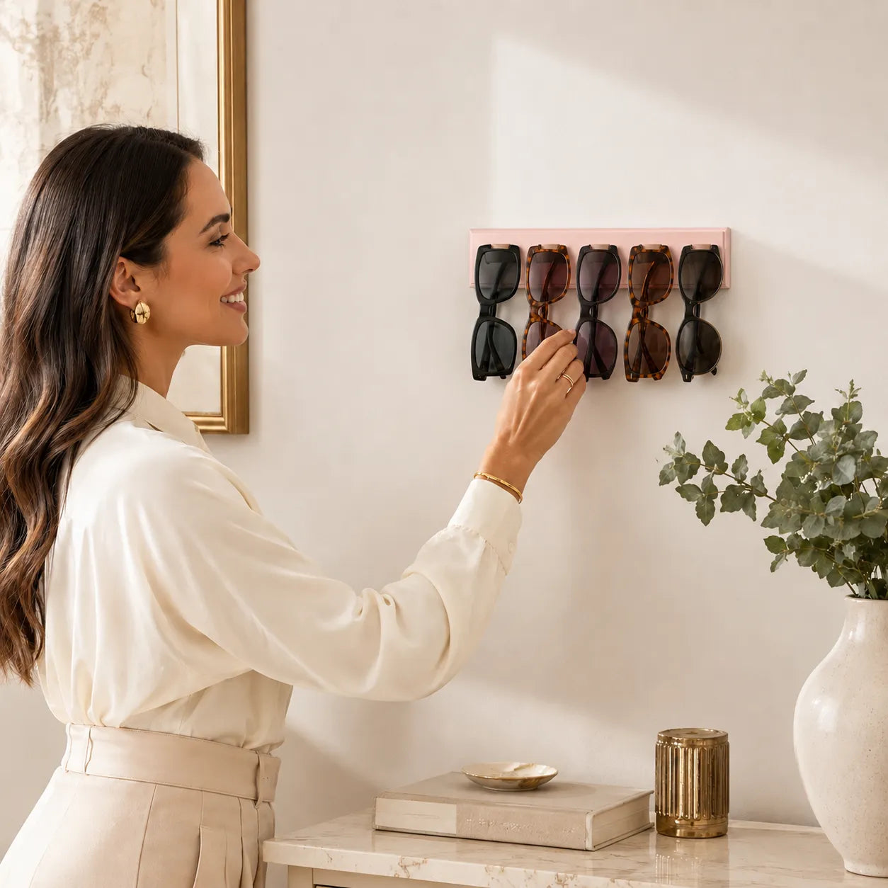 Woman hanging a pink sunglasses holder on a wall with sunglasses inside.