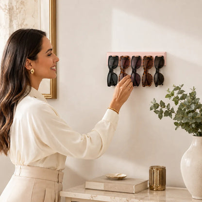 Woman hanging a pink sunglasses holder on a wall with sunglasses inside.