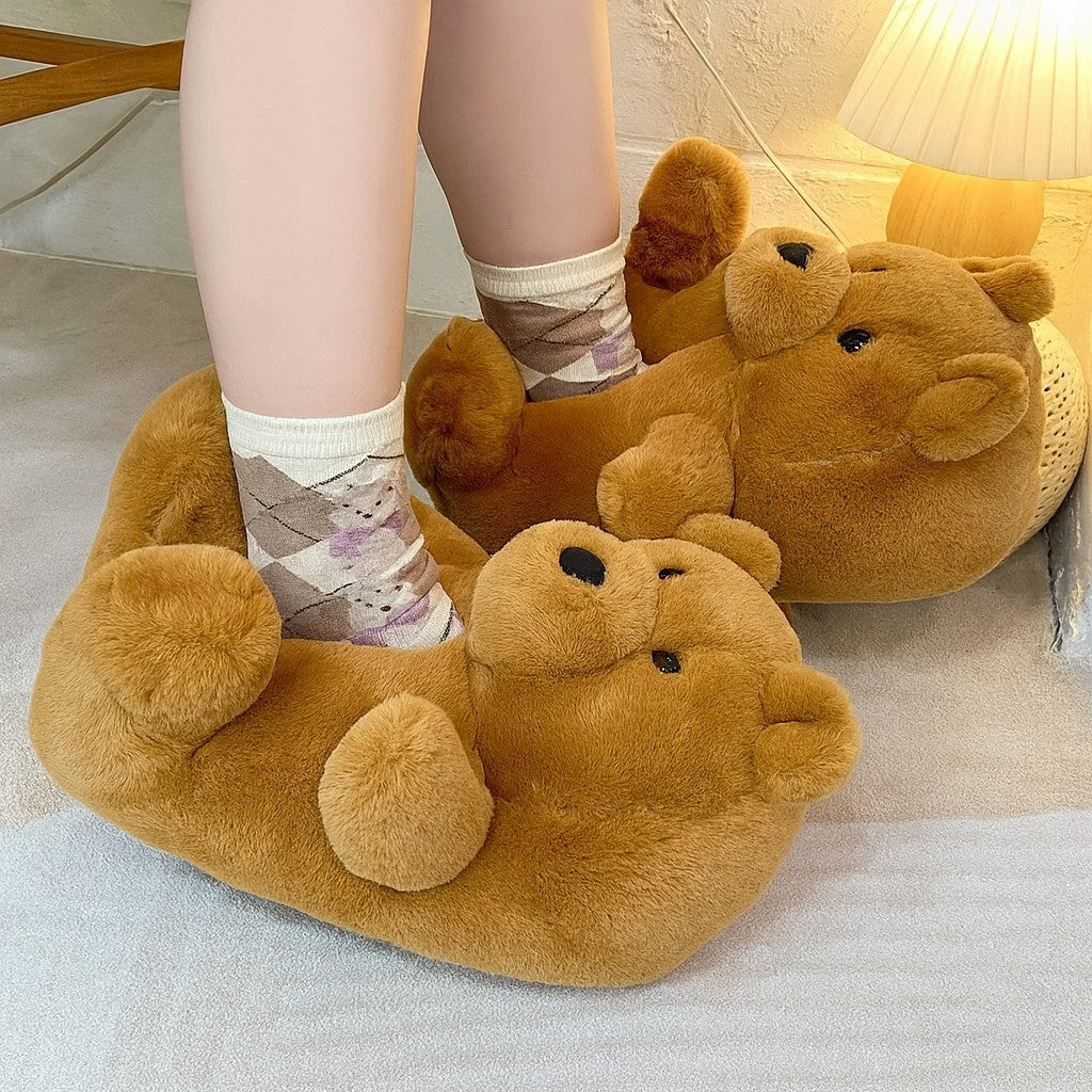 Brown bear-shaped slippers worn by a person on a light-colored floor.