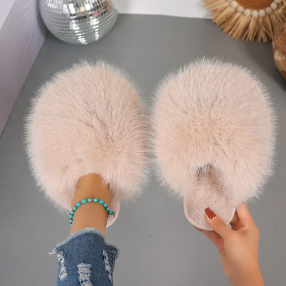 Pair of fluffy slippers held by a person on a gray surface with decorative items in the background.
