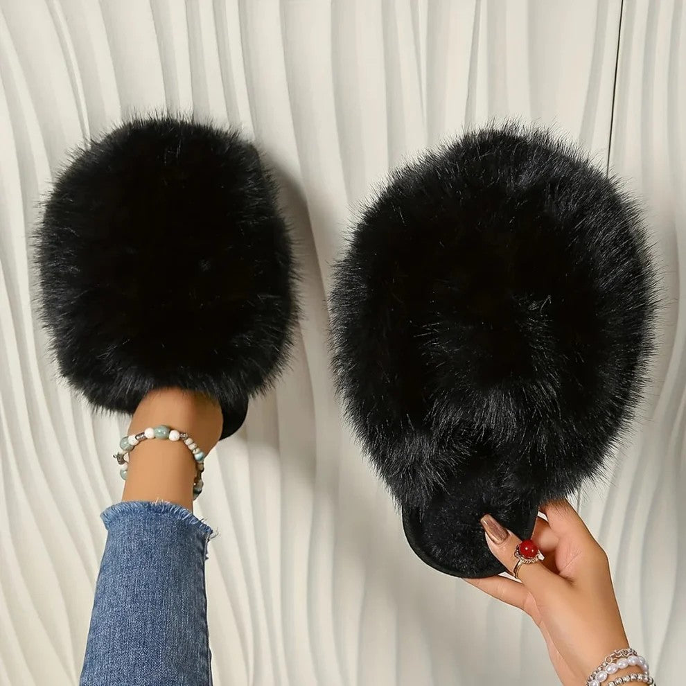 Black fluffy slippers being worn and held against a white background
