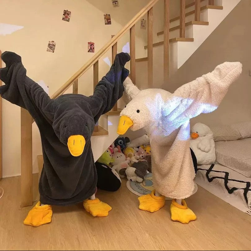 Two plush toys, one black and yellow, the other white with glowing wings, on a wooden floor.