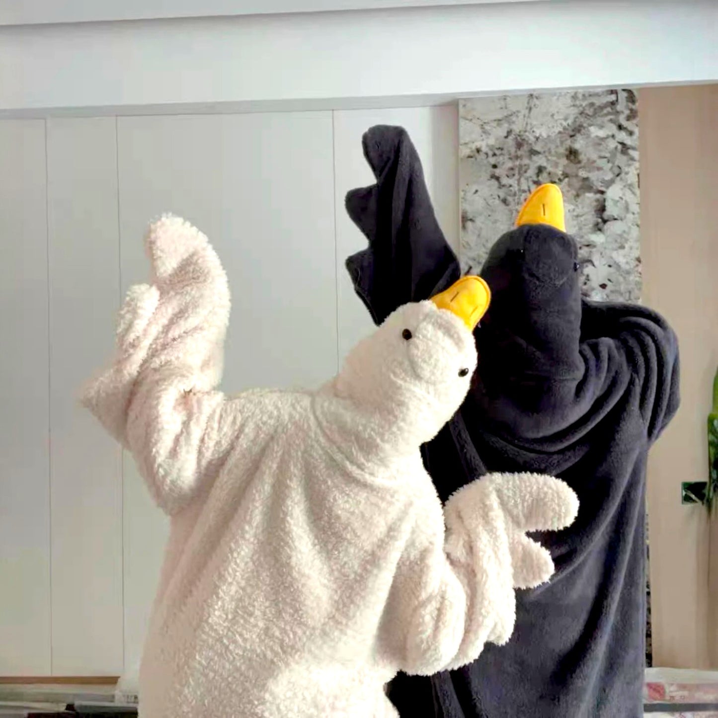 Two plush toys, one white and one black, with yellow beaks, on a surface.