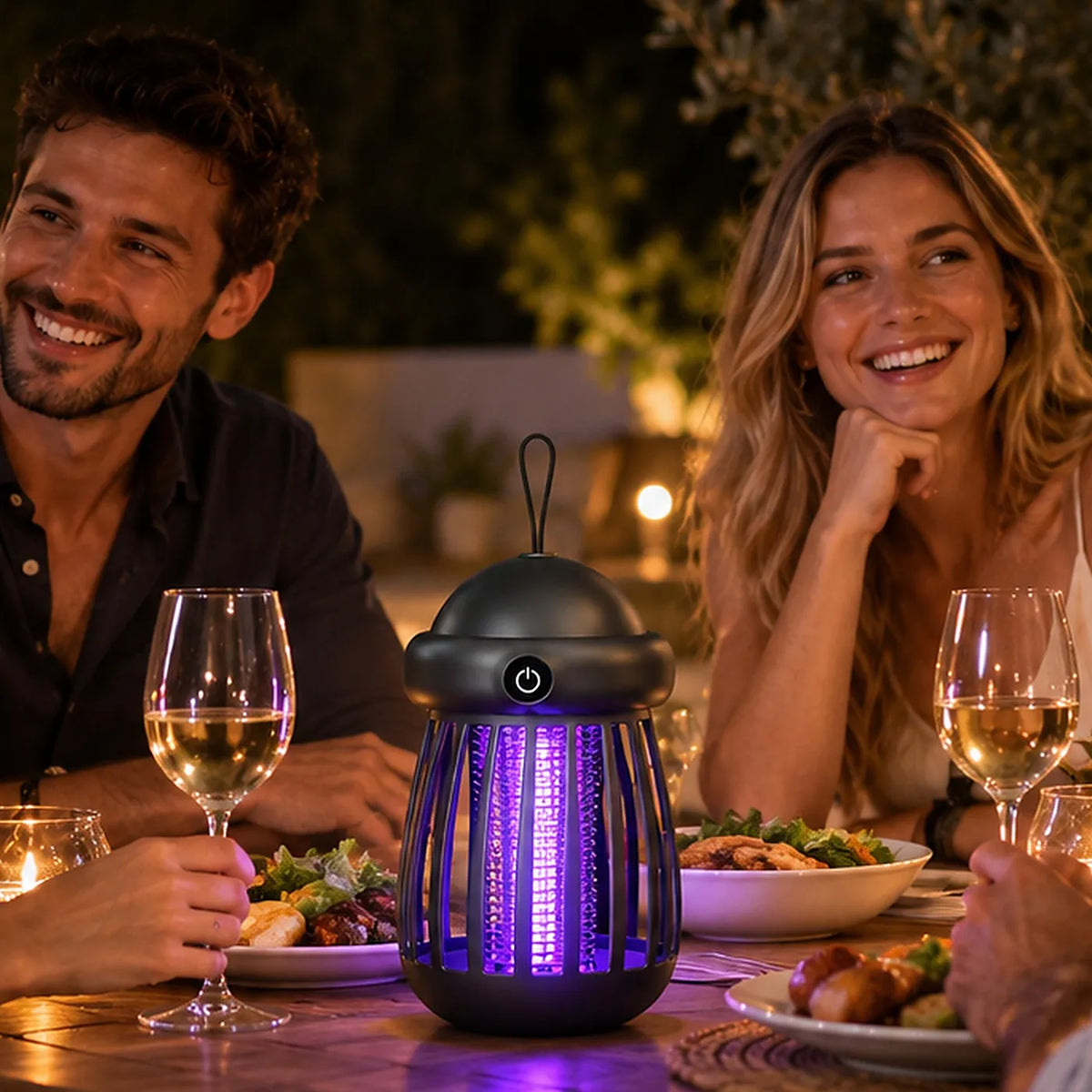 A black handheld insect killer light with glowing purple UV lights sits on a dinner table between a smiling man and a woman at an outdoor night dining event.