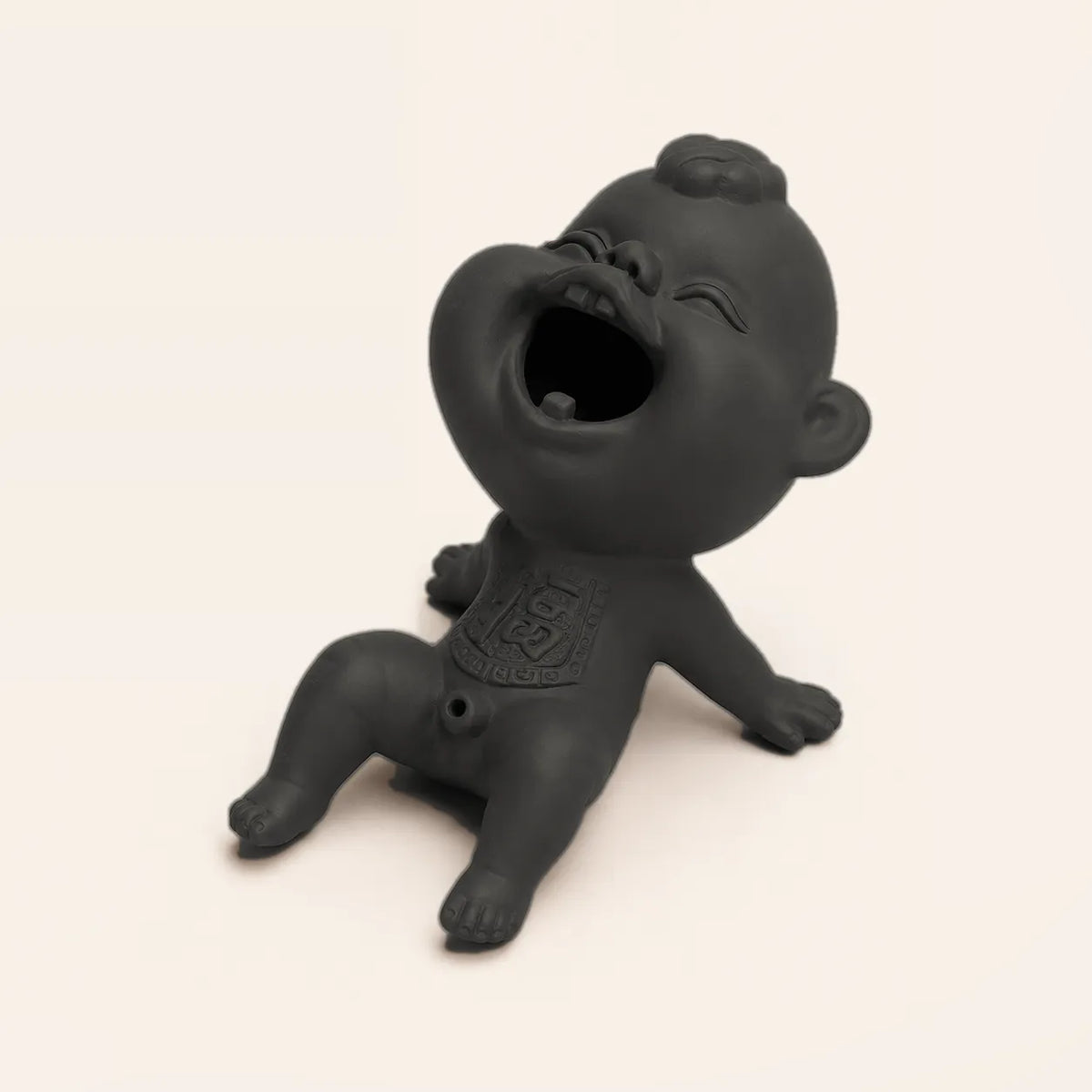A matte black ceramic laughing baby figurine sitting on a light beige background.