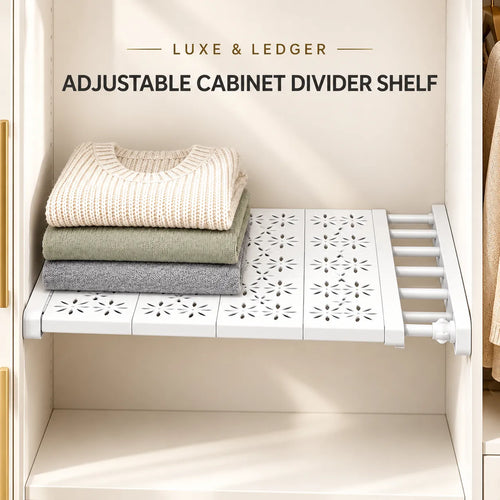 White adjustable cabinet divider shelf mounted inside a closet, holding three folded sweaters in cream, sage green, and gray. Text at the top reads 'LUXE & LEDGER ADJUSTABLE CABINET DIVIDER SHELF'.
