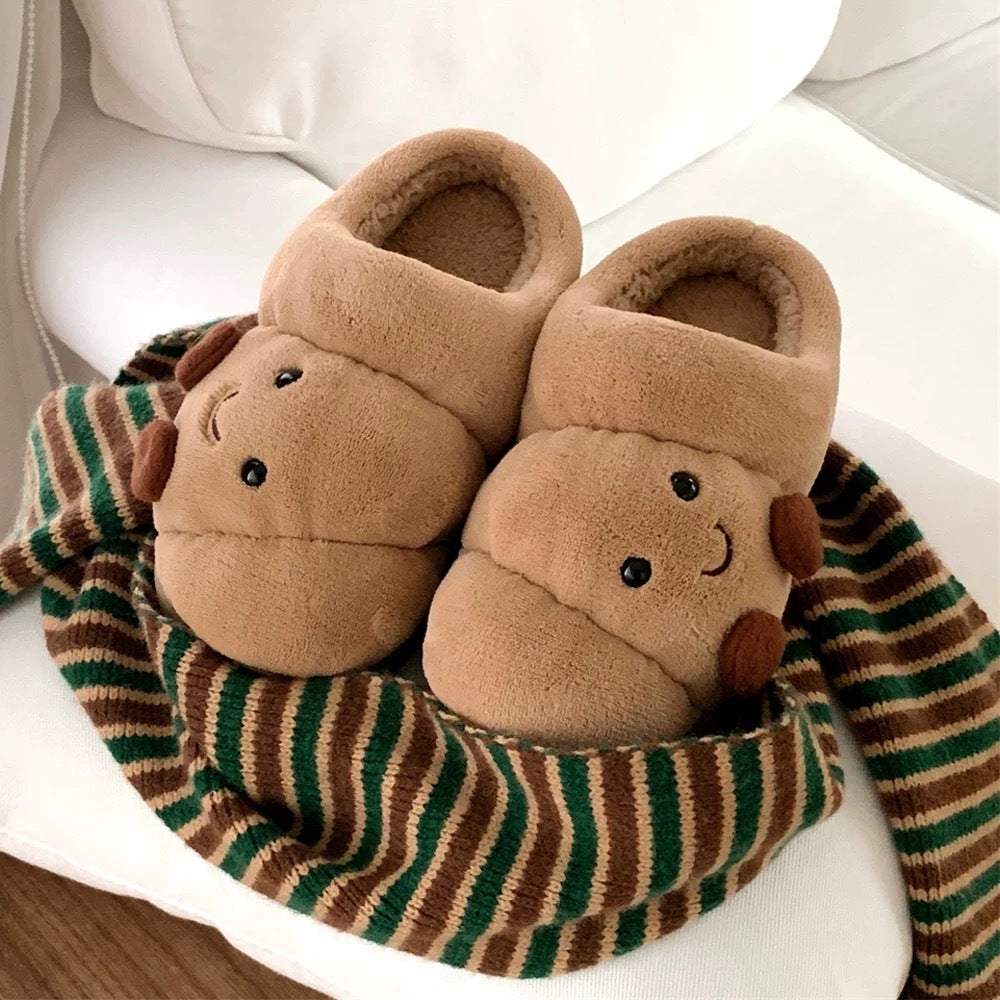 Pair of brown slippers with bear face design on a striped green and brown blanket.