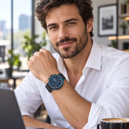 A man in a white button-down shirt wearing a blue and black chronograph watch, sitting at a desk with a laptop and coffee cup in a bright, modern office setting.