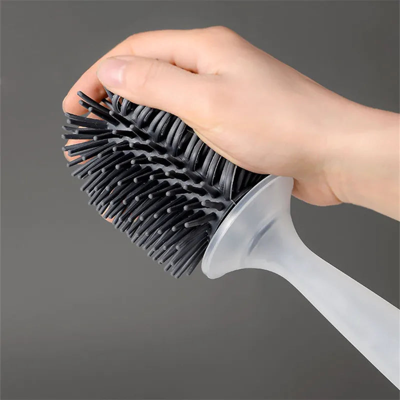 A hand holding a large black cleaning brush with dense bristles and a translucent white handle against a dark gray background.
