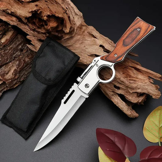 Folding knife with wooden handle and black sheath on a dark surface with wood and leaves.