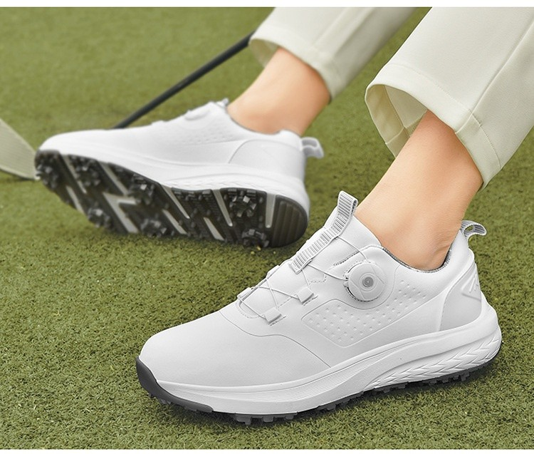 A pair of white golf shoes with a non-slip rubber sole, designed for all-terrain play on a green surface with golf balls and clubs in the background.