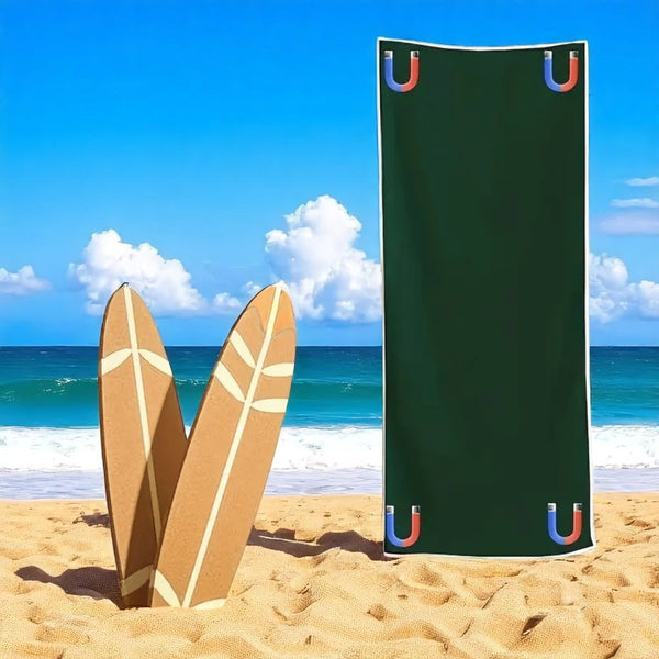 Green beach towel with colorful 'U' logos on a sandy beach with surfboards.