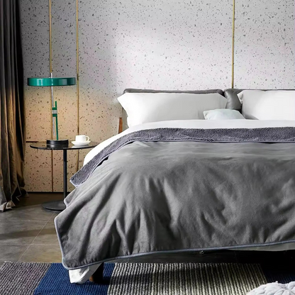 Bedroom with a bed covered in gray bedding, a side table with a lamp, and a textured wall.