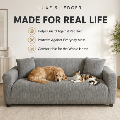 A gray textured slipcover fitted on a three-seat sofa in a bright living room, with a golden retriever lying on the left side and a calico cat lying on the right side. Large text at the top reads 'LUXE & LEDGER MADE FOR REAL LIFE' with three feature icons and descriptions about guarding against pet hair, protecting against everyday mess, and comfort for the whole home.