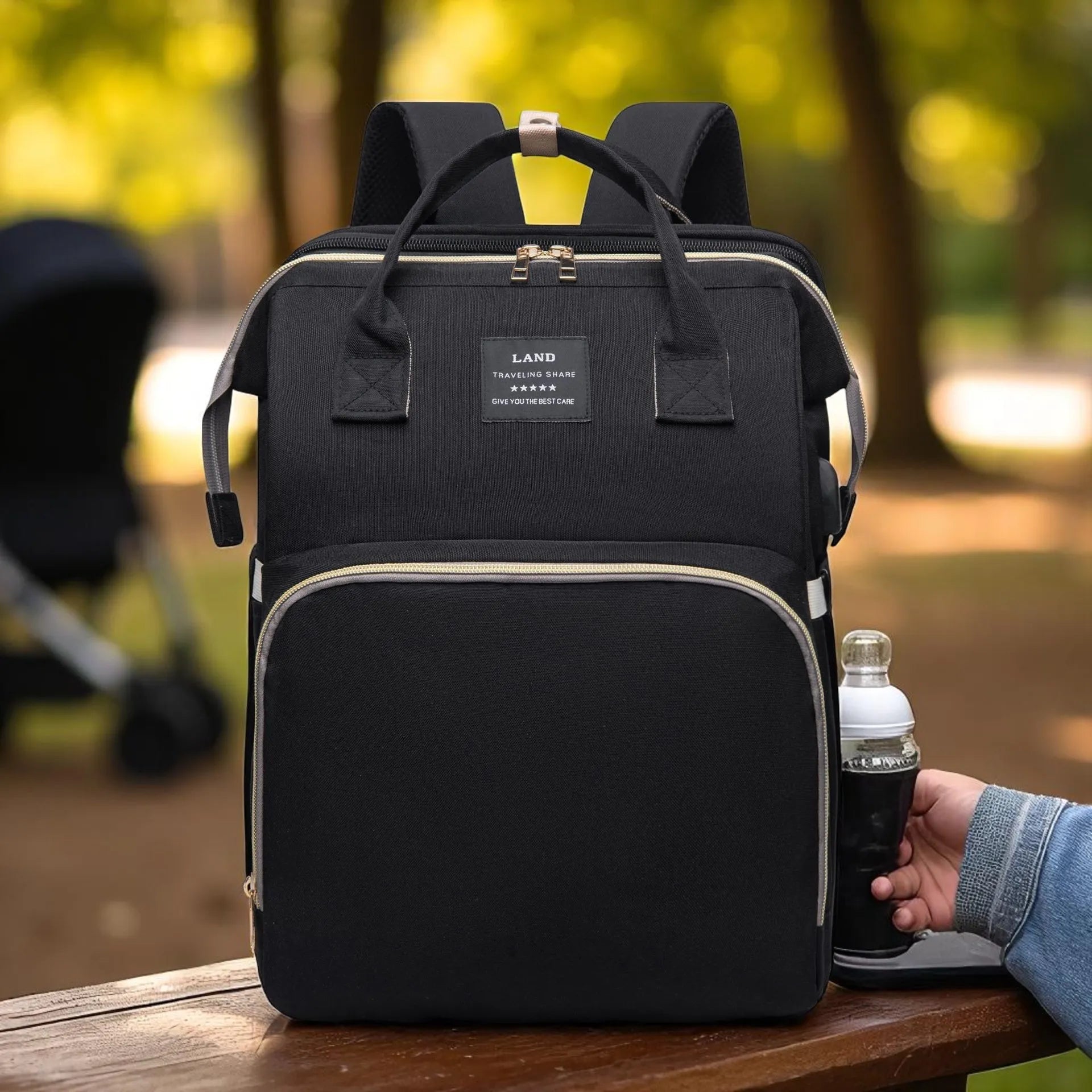 Black backpack with a hand holding a bottle of water in a park setting