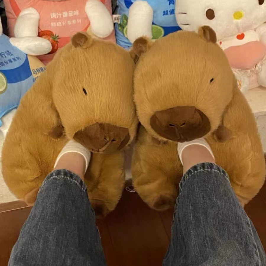 Brown dog-shaped slippers worn with jeans on a wooden floor, with plush toys in the background.