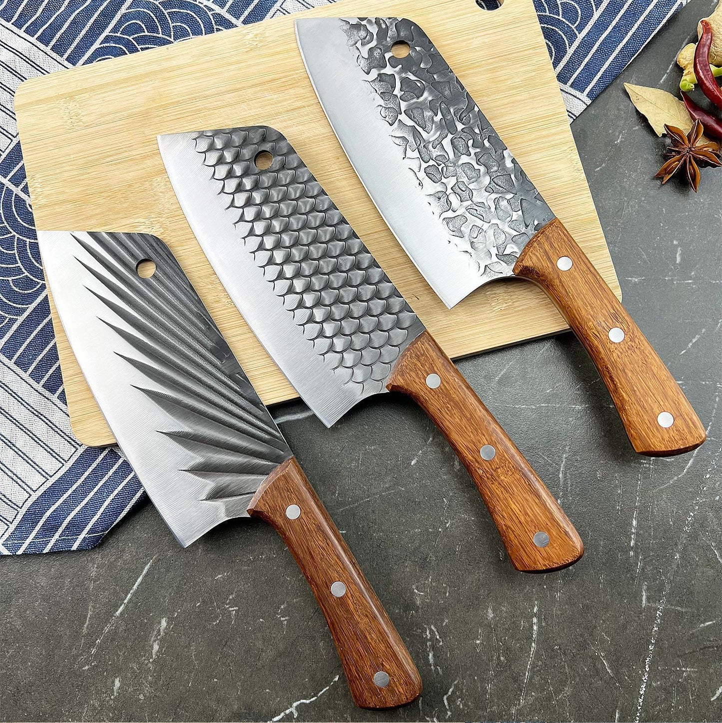 Three chef's knives with wooden handles on a wooden cutting board against a patterned cloth background.