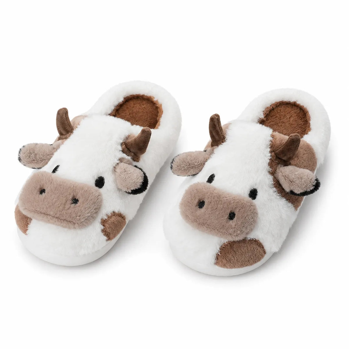 A pair of plush cow slippers on a clean white background. The slippers are primarily white with brown spots, featuring a raised cow face on the top with brown horns, a brown snout, and small black eyes.