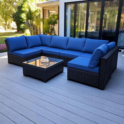 A rattan garden lounge set with blue cushions, including a sofa and a table, placed on an outdoor patio.