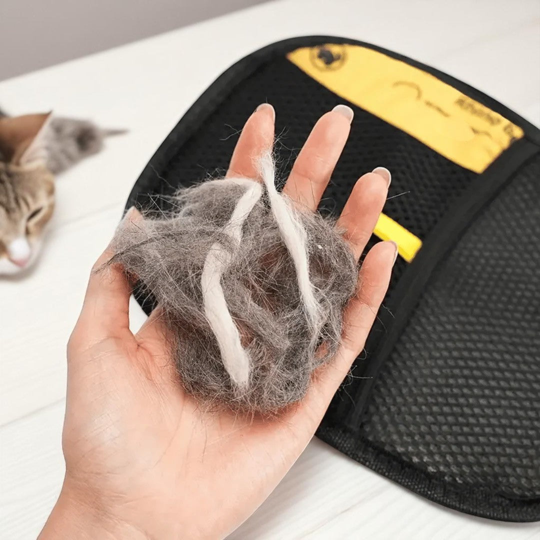 Person holding pet hair collected with a grooming tool, with a cat in the background.