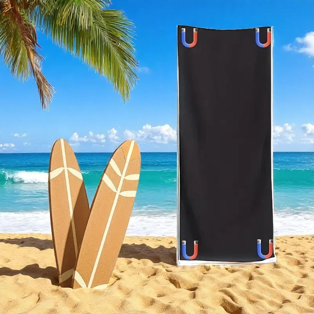 Black towel with U-shaped hooks on a sandy beach with surfboards and palm trees.