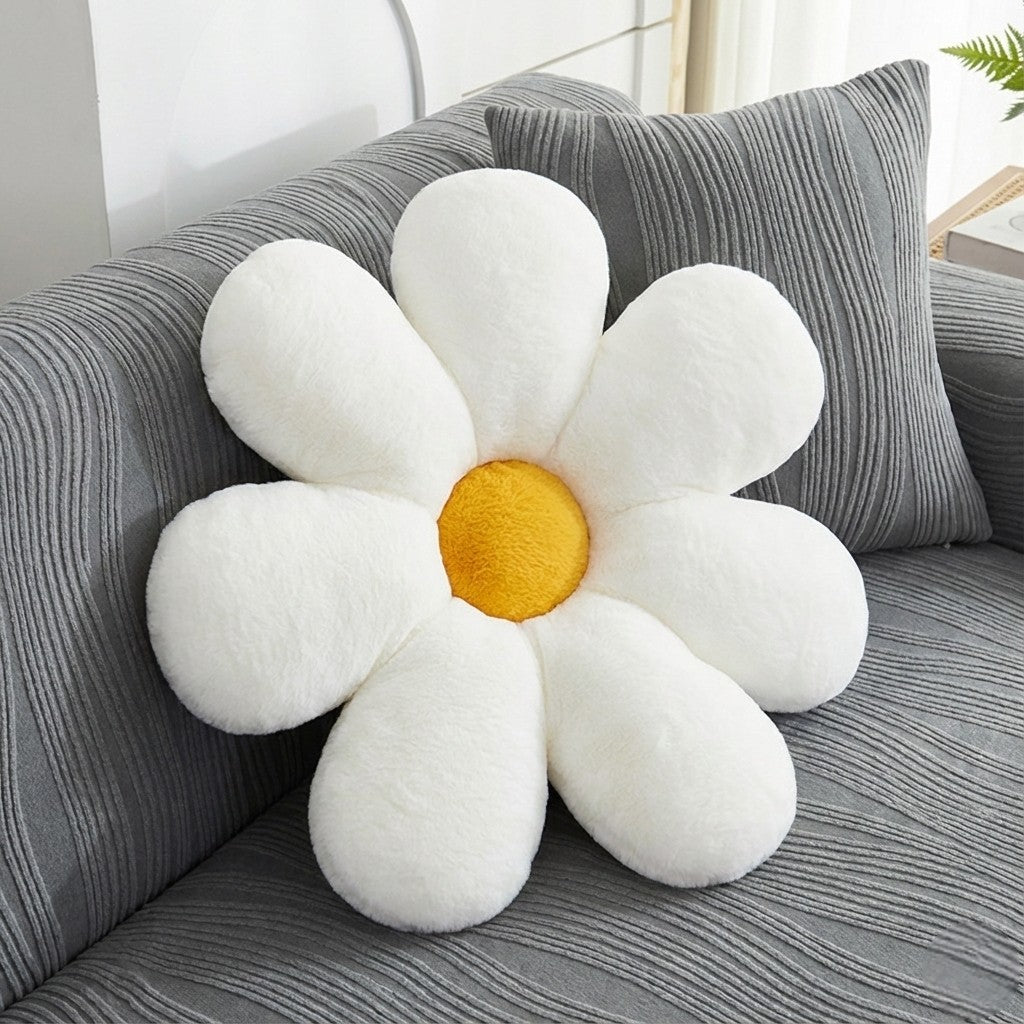 Flower-shaped pillow with white petals and a yellow center on a gray couch.