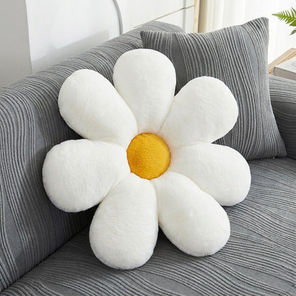 Flower-shaped pillow with white petals and a yellow center on a gray couch.