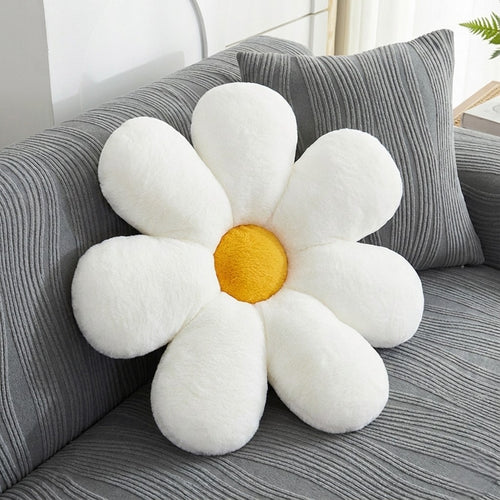 Flower-shaped pillow with white petals and a yellow center on a gray couch.