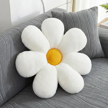 A plush daisy-shaped throw pillow with white petals and a yellow center, resting on a gray striped sofa next to a matching pillow.