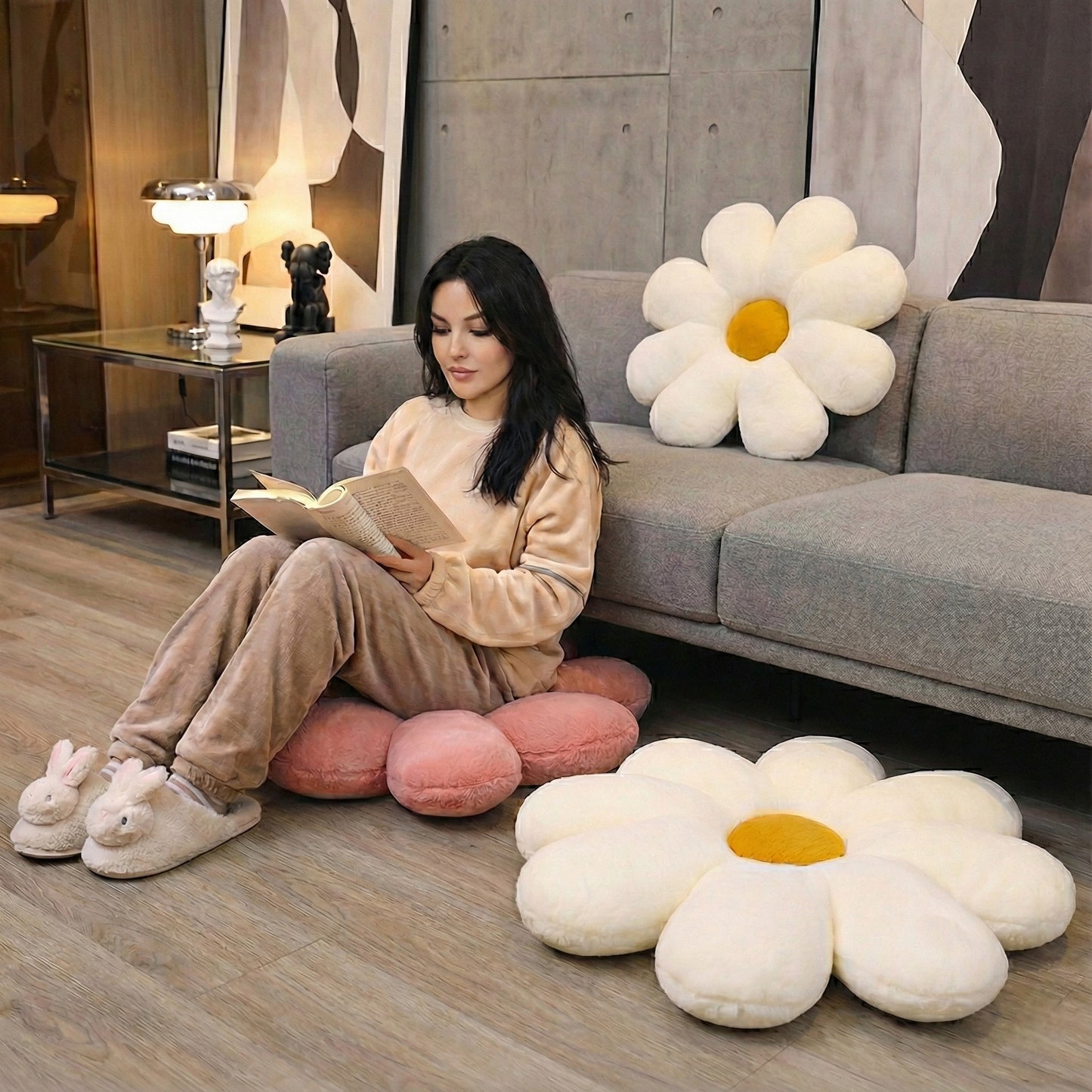 Woman reading a book on a gray couch with large flower-shaped cushions in a modern living room.
