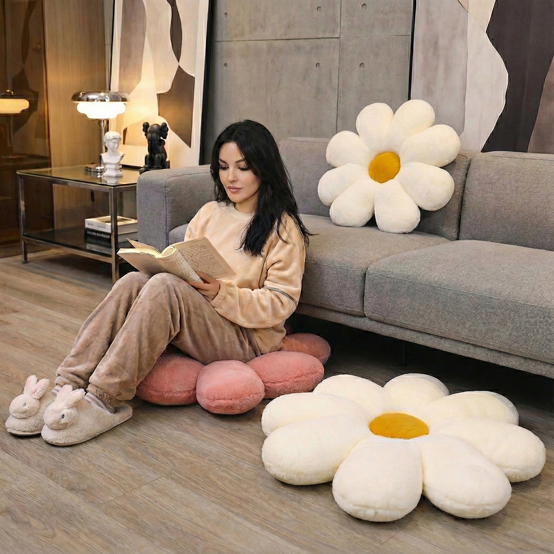 Woman reading a book on a gray couch with large flower-shaped cushions in a modern living room.