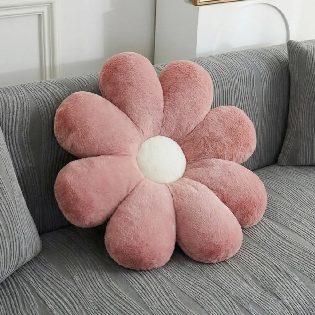 A pink flower-shaped plush throw pillow with a white center, resting on a gray textured sofa.
