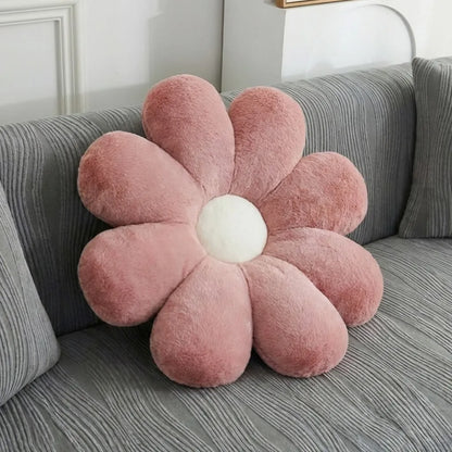 A pink flower-shaped plush throw pillow with a white center, resting on a gray textured sofa.