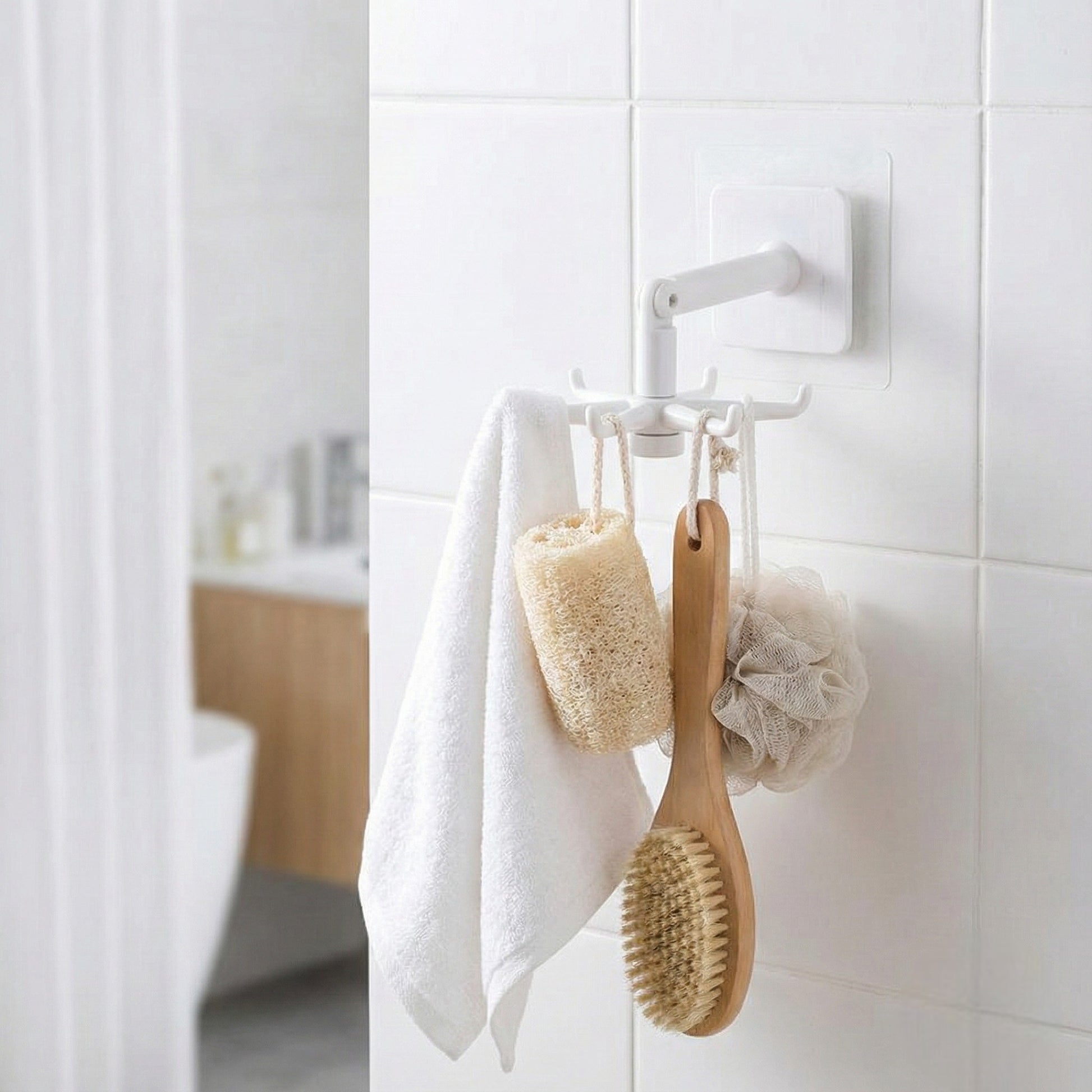 White wall hook with a towel, sponge, and brush on a tiled bathroom wall.