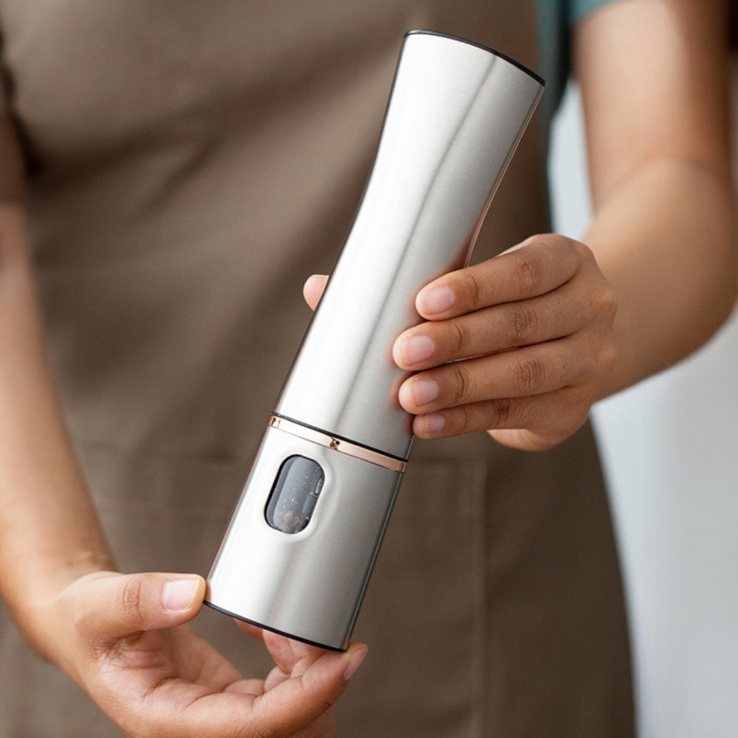 Hand holding a silver electric wine opener with a blurred background