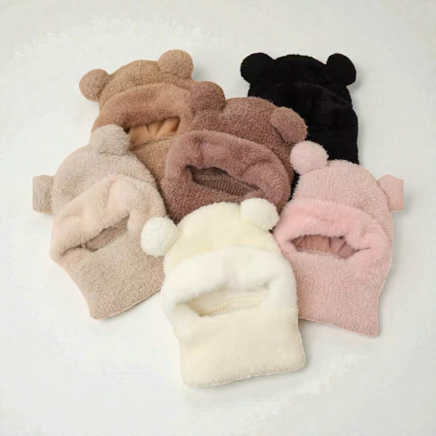 Set of five plush beanies with bear ears in various colors on a light gray background