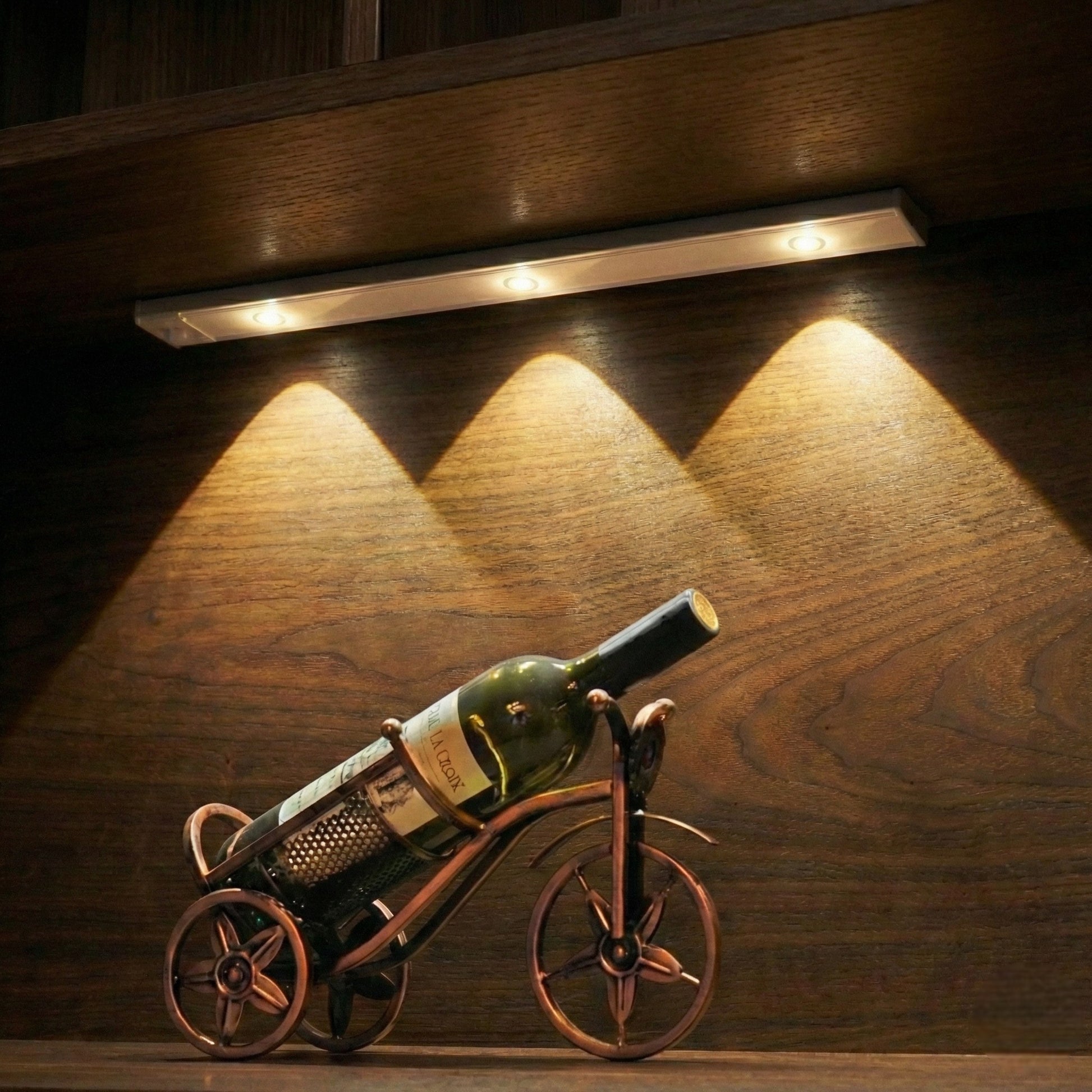 Wine bottle on a bicycle-shaped holder under a strip light on a wooden surface