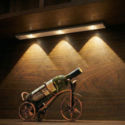 Wine bottle on a bicycle-shaped holder under a strip light on a wooden surface